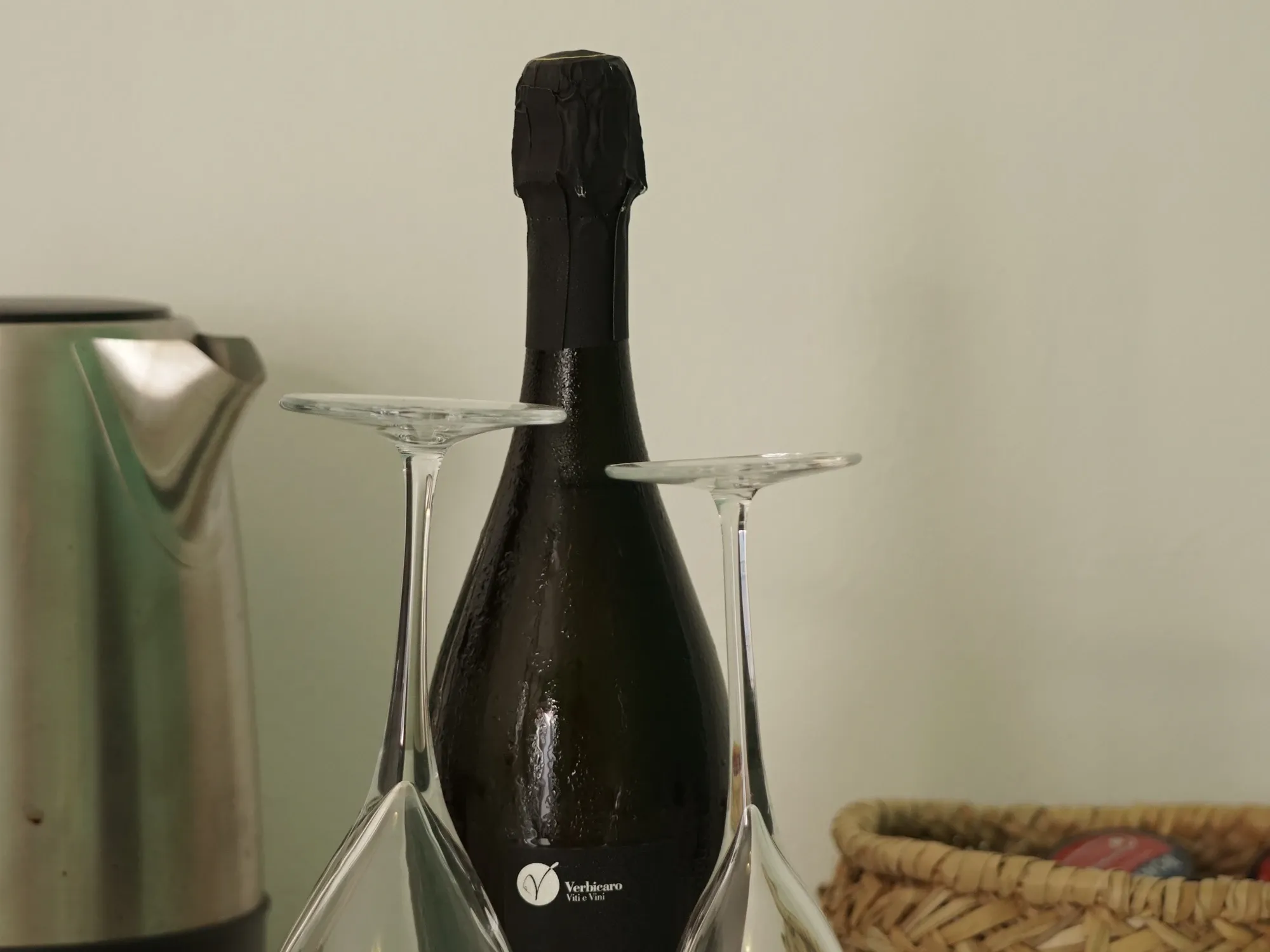 Botella de espumoso con dos copas boca abajo, hervidor y cesta de cápsulas