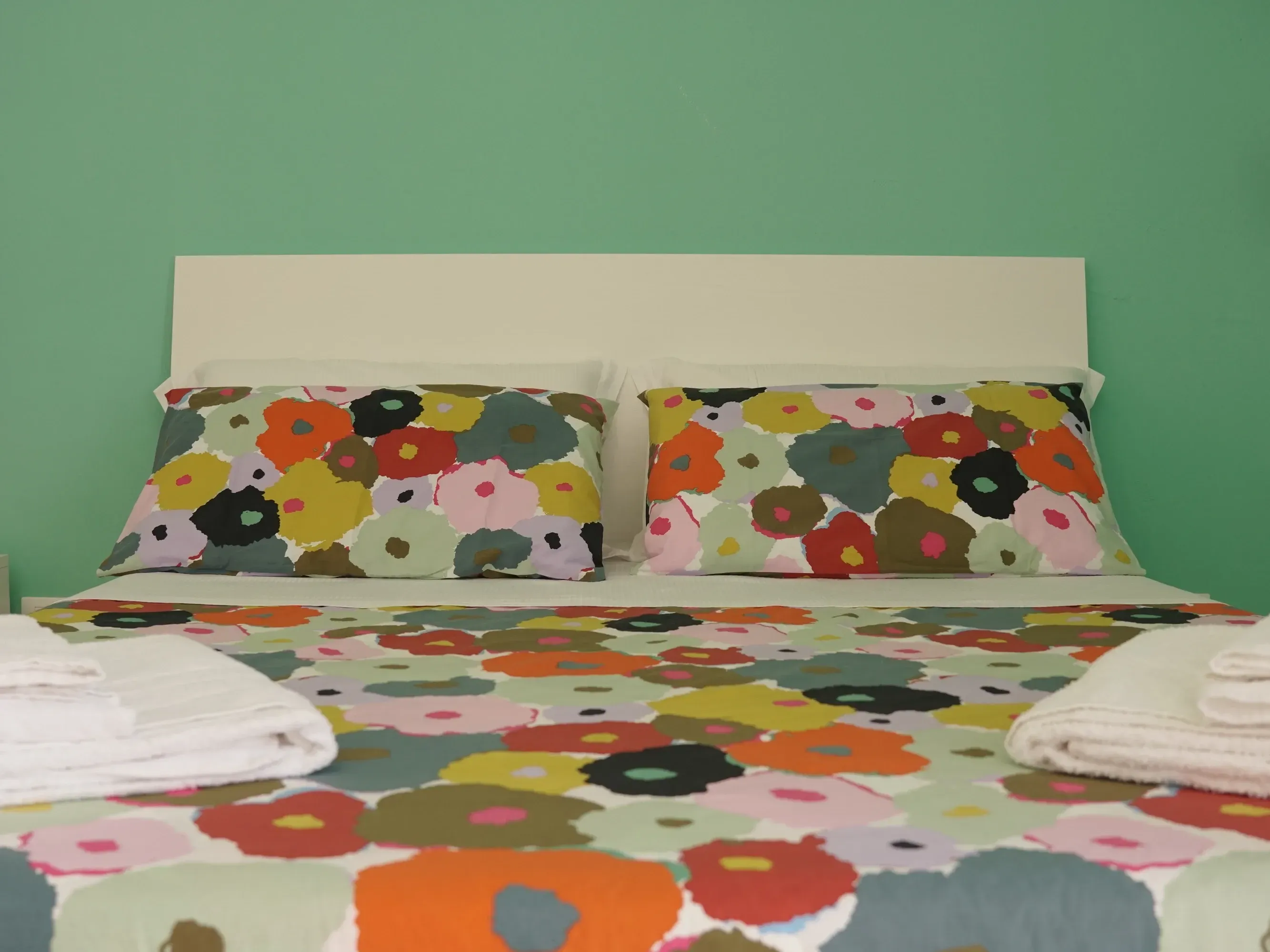 Cama doble con cabecero blanco, ropa de cama de flores y toallas, pared verde
