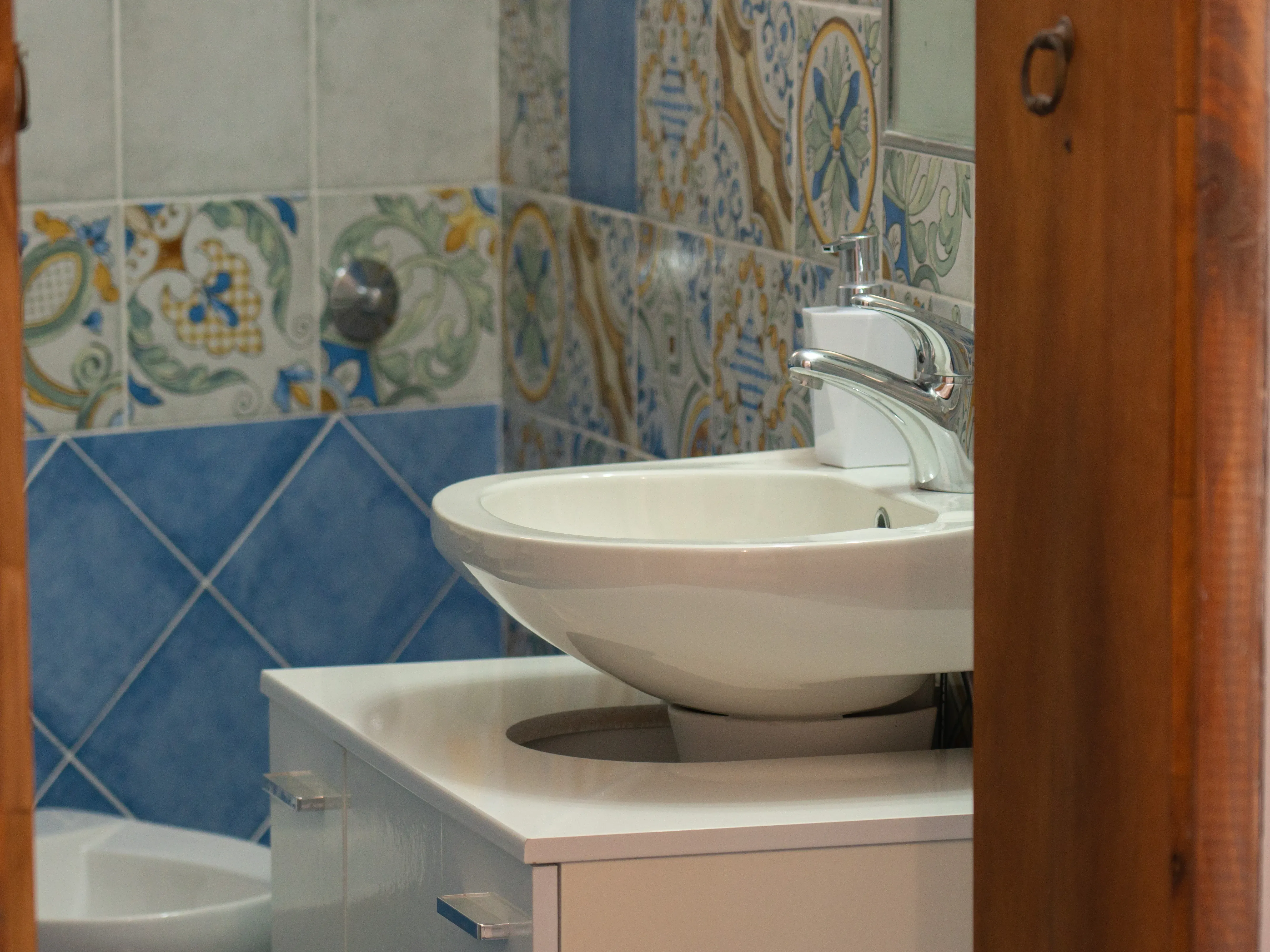 Lavabo blanco sobre mueble, baño con azulejos azules y decorados tipo mayólica